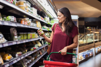 Young woman shopping in grocery store. Mature woman checking food label in supermarket. Latin woman holding shopping basket and choose a product in supermarket.